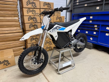 Small dirt bike on a stand in front of stacked boxes with branding.