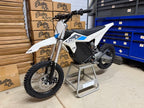 Small dirt bike on a stand in front of stacked boxes with branding.